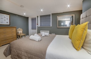 Un dormitorio con una cama grande, un aparador de madera, una silla y una ventana con persianas.