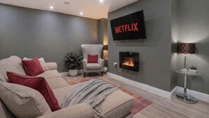A living room with a beige sofa, red pillows, a glass coffee table, a fireplace, and a wall-mounted TV displaying 'NETFLIX'. - Gillygate Boutique Apartment - sleeps 4 guests  in 1 bedroom (York)