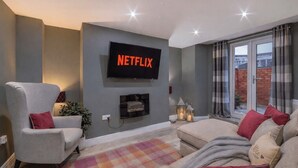 A living room with a flat-screen TV mounted on the wall, a grey armchair, a sofa, and a colorful rug. - Gillygate Boutique Apartment - sleeps 4 guests  in 1 bedroom (York)