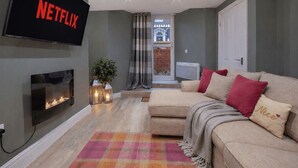 Una sala de estar con televisor de pantalla plana, chimenea, sofá con cojines y una alfombra colorida.