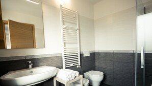 A modern bathroom with a white sink, a toilet, and a glass shower enclosure. - Apartment with terrace (Campoformido Udine)