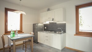 A modern kitchen with white cabinets, a stainless steel refrigerator, a gas stove, and a window providing natural light. - Apartment with terrace (Campoformido Udine)