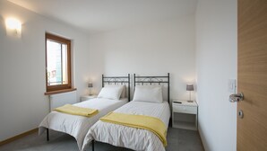 A bedroom with two single beds, a window, bedside tables with lamps, and a door. - Apartment with terrace (Campoformido Udine)