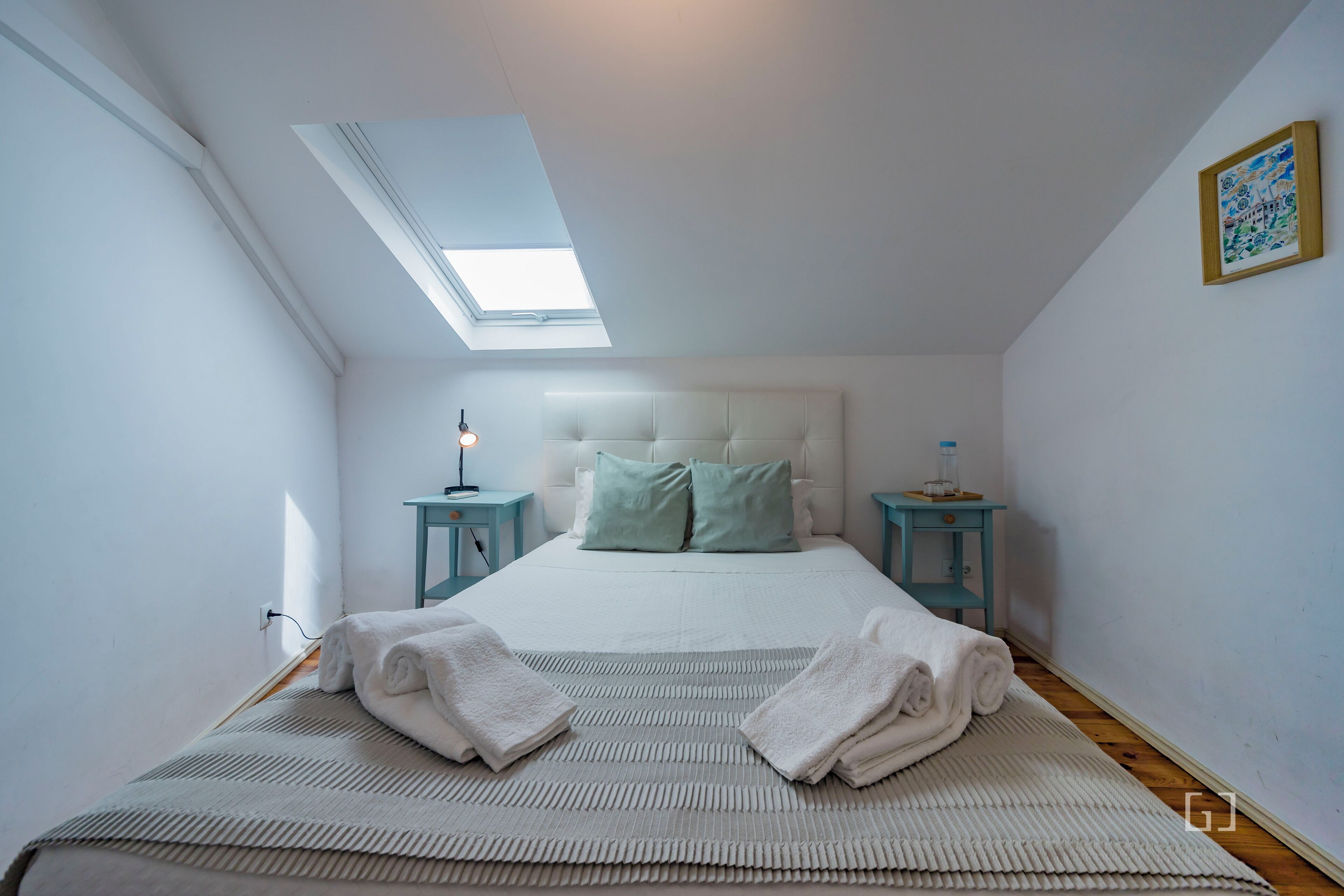 Une chambre avec une lucarne, un lit avec des oreillers, deux tables de chevet et des serviettes sur le lit.