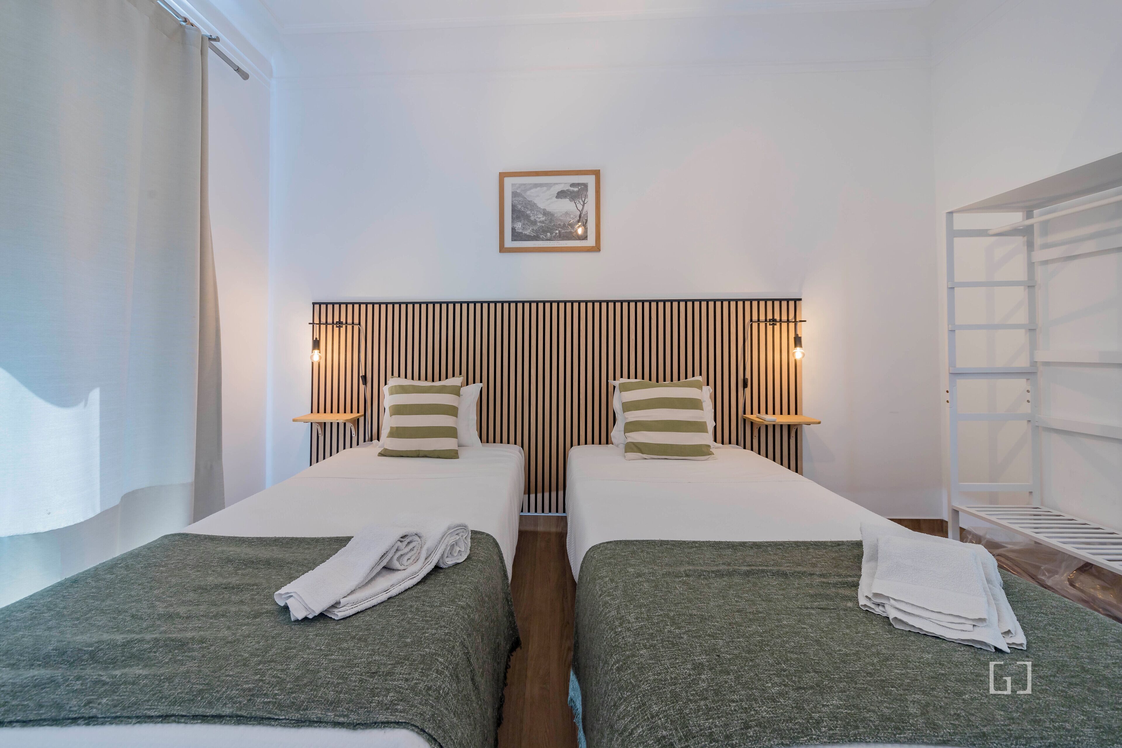 Habitación de hotel con dos camas, cabecero de listones de madera, un cuadro enmarcado en la pared y un estante blanco.