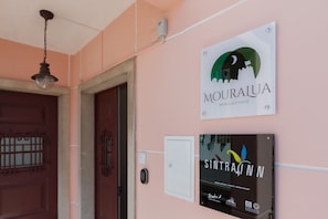 Cartell del llindar de l'alberg 'MOURALIA' i 'SINTRAINN', amb una porta i una làmpada penjant a la paret.