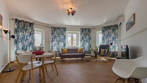 A spacious living room with a wooden floor, a round dining table, a sofa, and a TV. - MouraLua (Sintra)