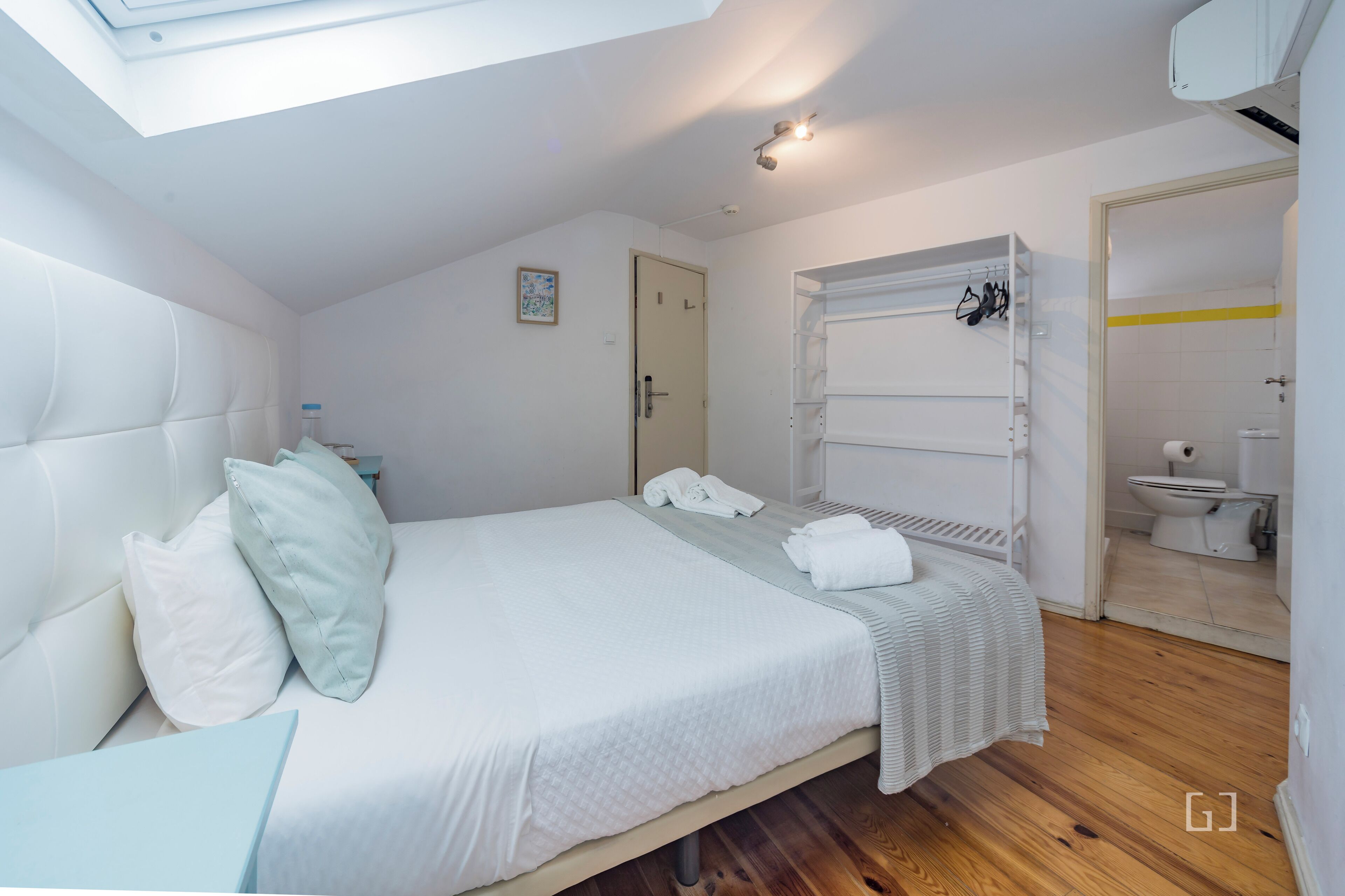 A bedroom with a bed, pillows, a bedside table, a wardrobe, and a bathroom visible through an open door.
