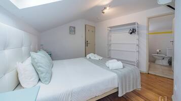 A bedroom with a bed, pillows, a bedside table, a wardrobe, and a bathroom visible through an open door.