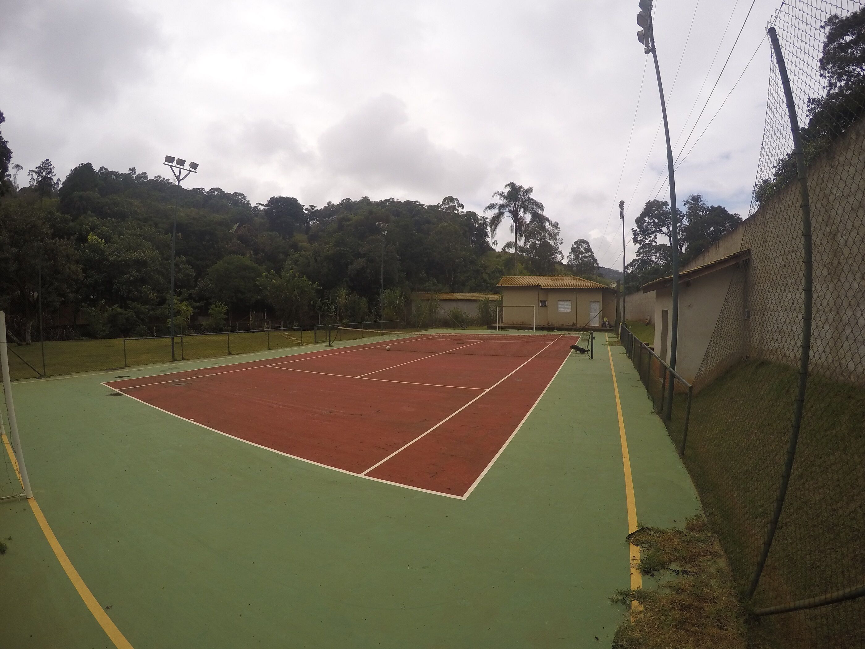 A tennis court with a net, surrounded by a fence and trees.