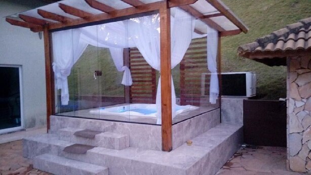 Ett bubbelbad med en glasvägg och en träpergola, omgivet av stentrappor och en stenmur.