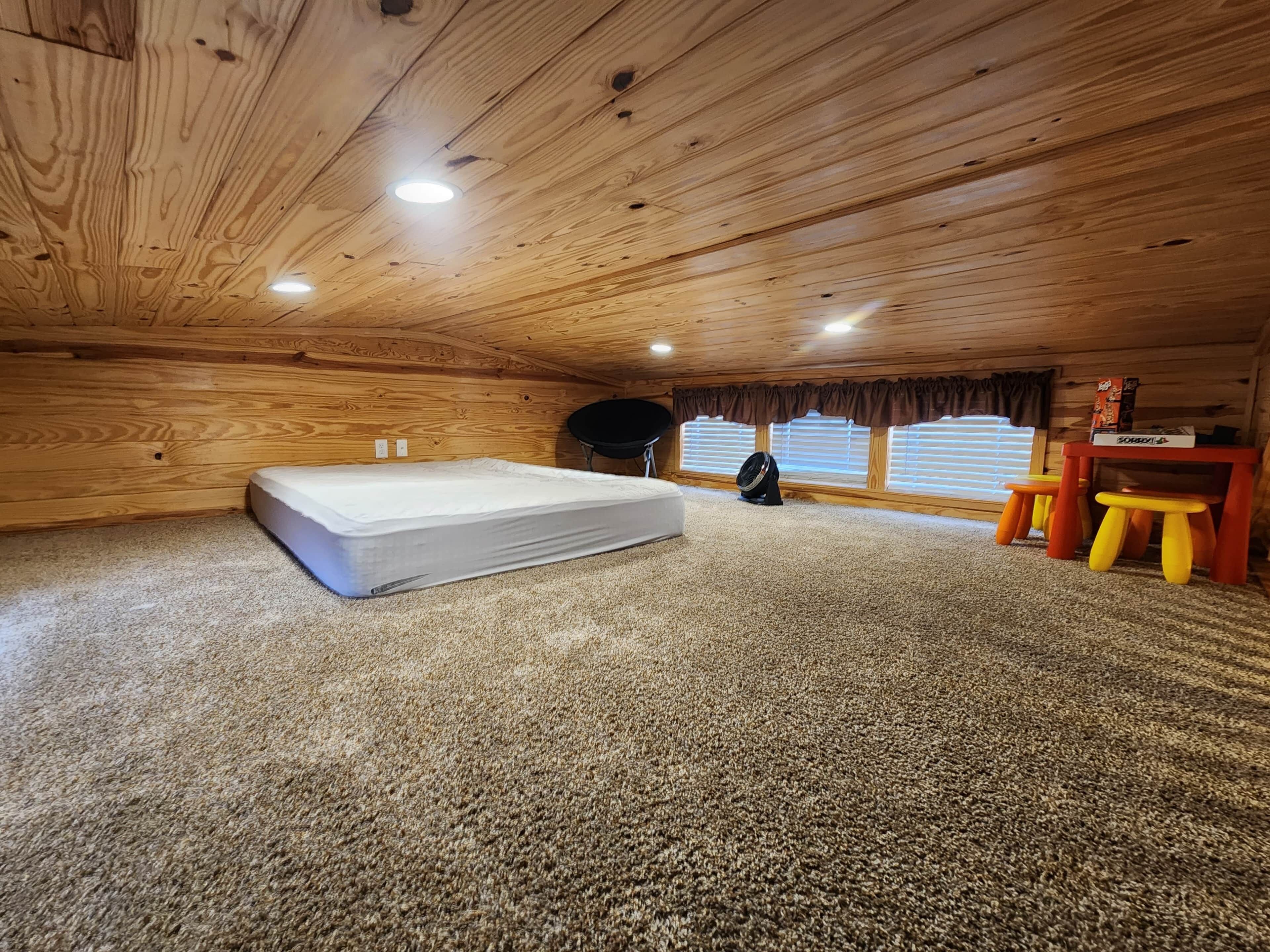 A cozy attic bedroom with a large mattress, a small desk, and a chair.