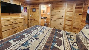 Quarto de cabana de madeira com cama, penteadeira e televisão.