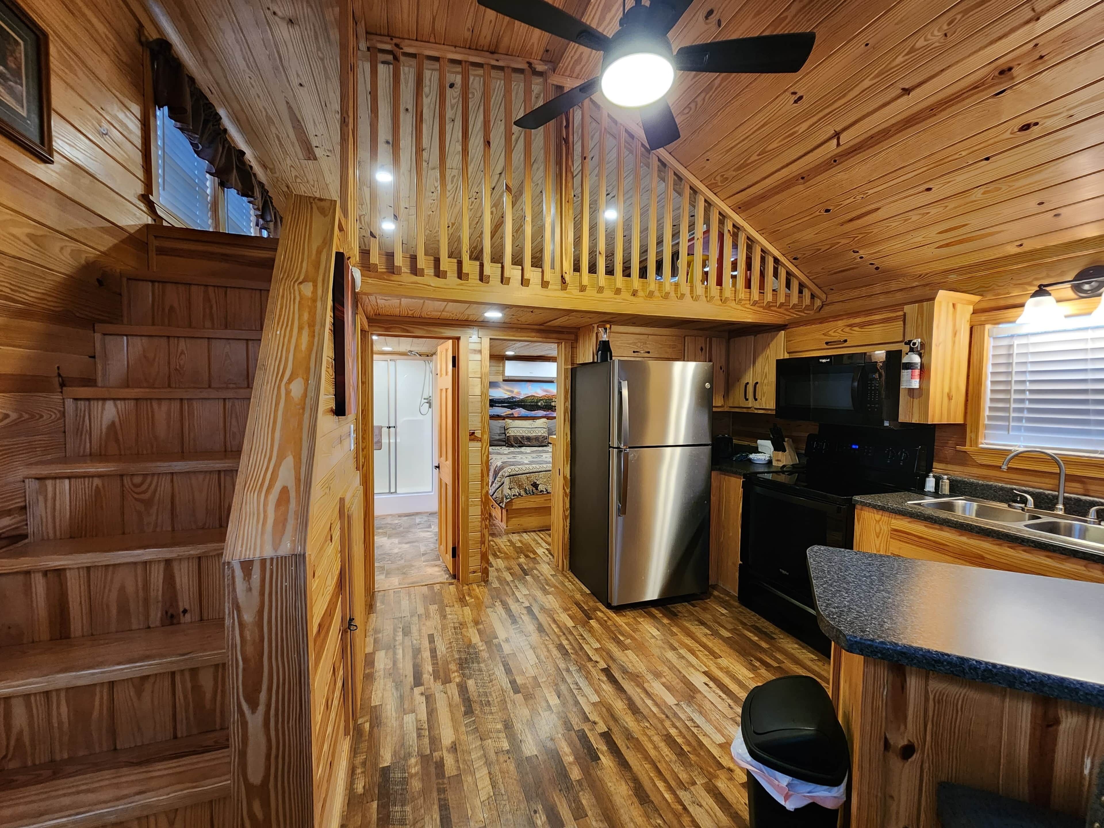 L’intérieur d’une cabane en bois comprend une cuisine, un réfrigérateur, un four à micro-ondes et un escalier menant à une zone douche.