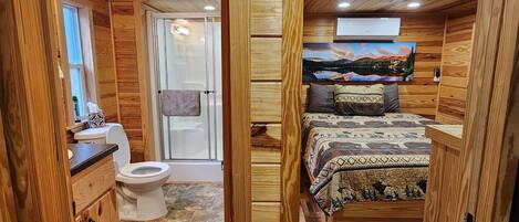 A compact, wood-paneled room with a bed, a toilet, and a small kitchenette.