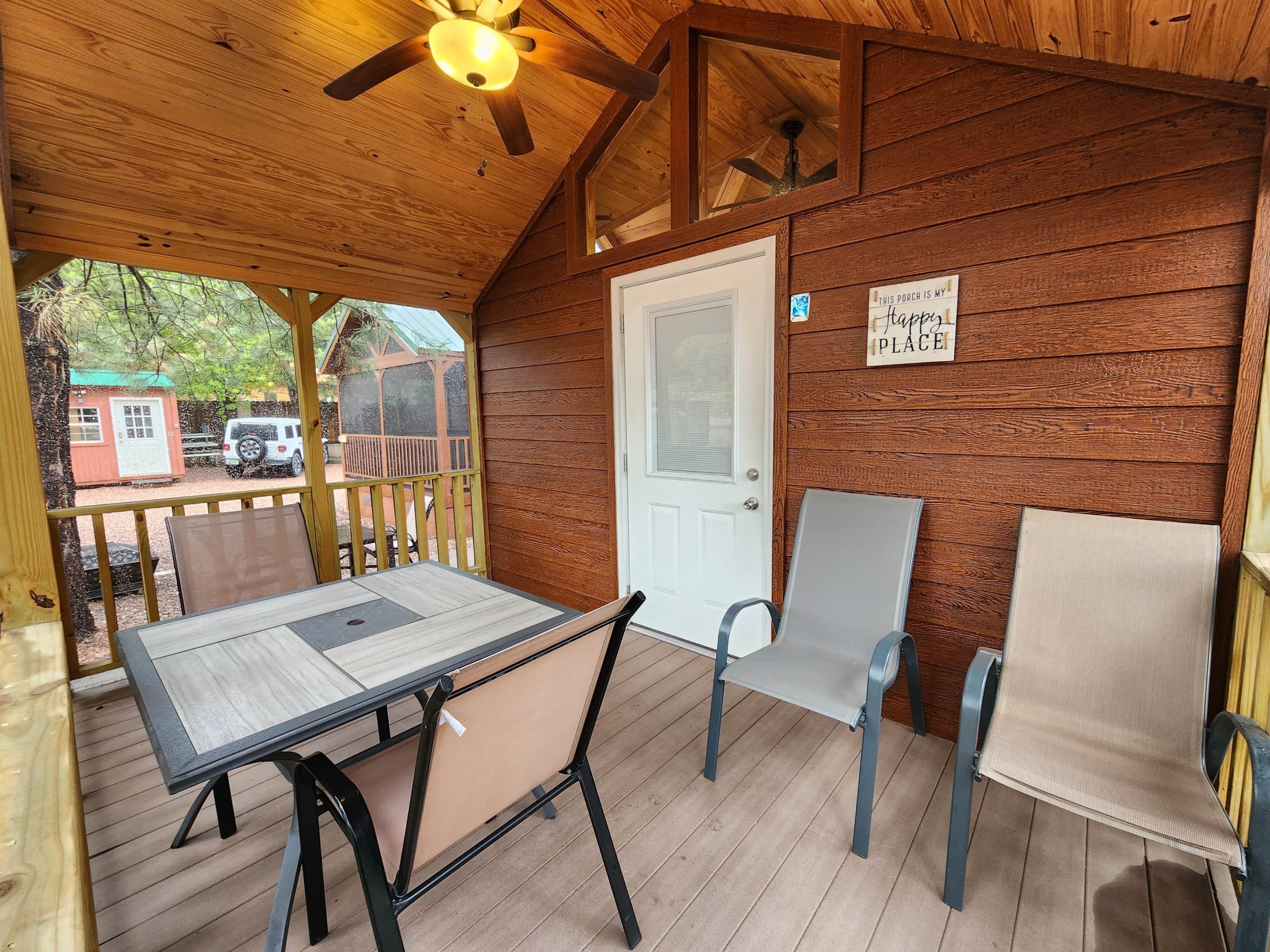 A wooden porch with a table and chairs, a ceiling fan, and a door.