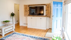 Een kamer met een houten tv-meubel, een blauwe deur en een witte bank met een plant.