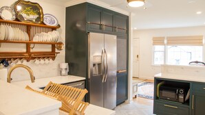 Een moderne keuken met een roestvrijstalen koelkast, houten planken met servies, een houten droogrek en een magnetron in een kast.
