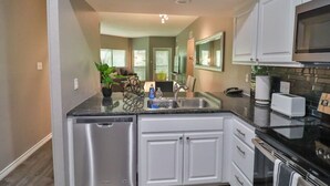 A compact kitchen with white cabinets, a stainless steel dishwasher, a built-in oven, and a microwave.