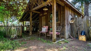 A rustic wooden cabin with a porch, two chairs, and a table. - Farmhouse on Vineyard (Redwood Valley)
