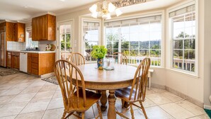 A kitchen with wooden cabinets, a dining table with chairs, and a view of the outdoors through large windows. - Farmhouse on Vineyard (Redwood Valley)