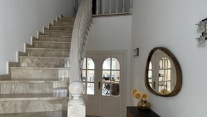 A staircase with a white balustrade leading to a second floor. A round mirror and a vase with flowers are on a console table beside the stairs. - Beautiful villa on wide canal with 15m mooring and pool! (Empuriabrava)