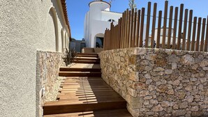 A set of wooden stairs leading up to a white building with a stone wall and a wooden fence. - Beautiful villa on wide canal with 15m mooring and pool! (Empuriabrava)