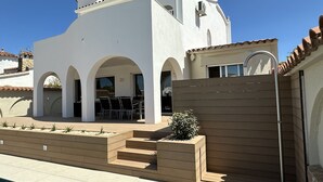 A modern white building with a pool, outdoor seating, and a wooden fence. - Beautiful villa on wide canal with 15m mooring and pool! (Empuriabrava)