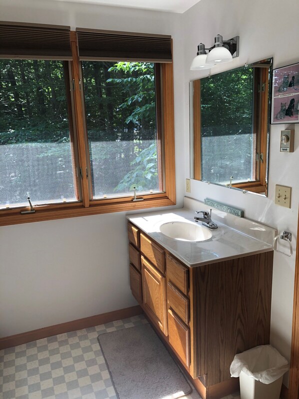 A bathroom with a wooden vanity, a white sink, a mirror, and a window with blinds.
