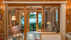 A wooden interior with a dining area, a table with chairs, a lamp, and a view of the sea through large glass doors.