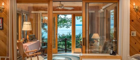 A wooden interior with a dining area, a table with chairs, a lamp, and a view of the sea through large glass doors.