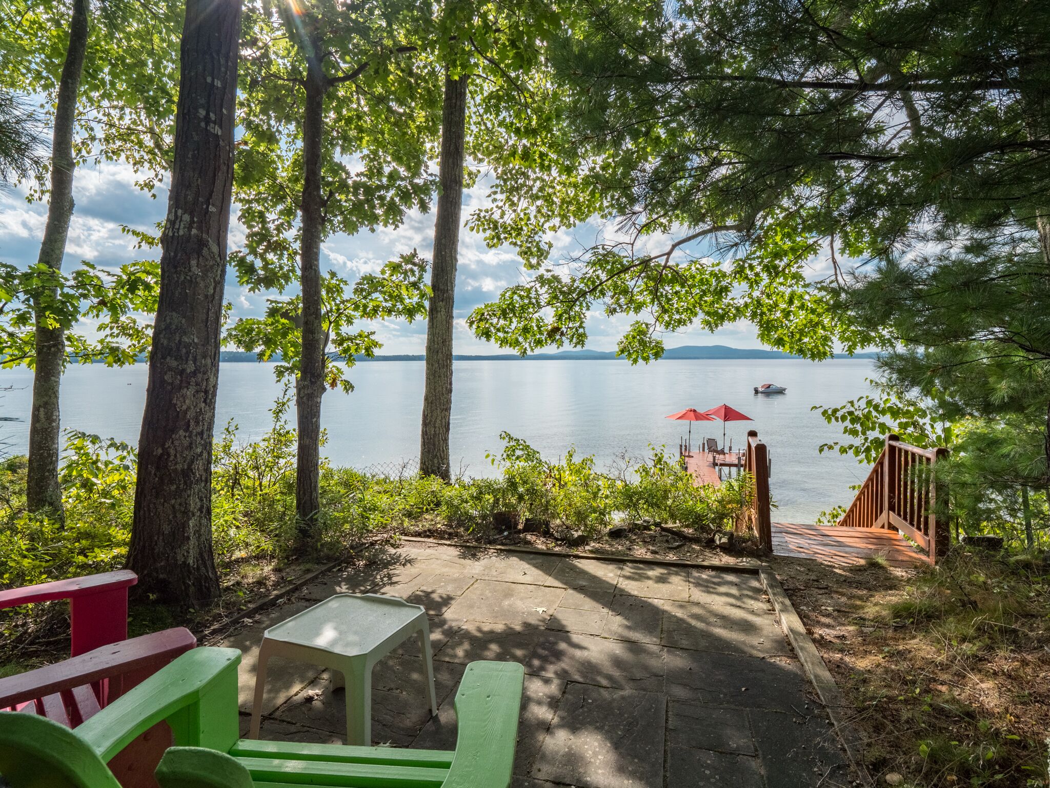 A lakeside patio with a table, chairs, and a red umbrella.