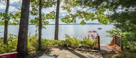 A lakeside patio with a table, chairs, and a red umbrella.