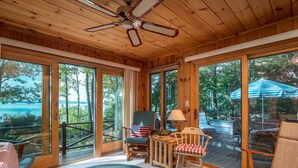 A wooden cabin interior with large windows, a ceiling fan, and a view of a lake.