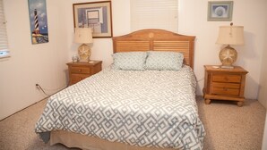 Un dormitorio con una cama de madera, dos mesitas de noche, una lámpara y un cuadro enmarcado en la pared.