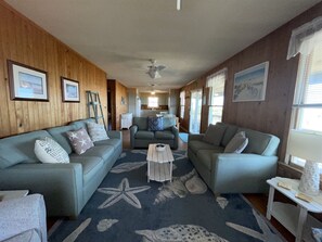 A cozy living room with a wooden interior, a starfish-patterned rug, and a kitchen in the background.