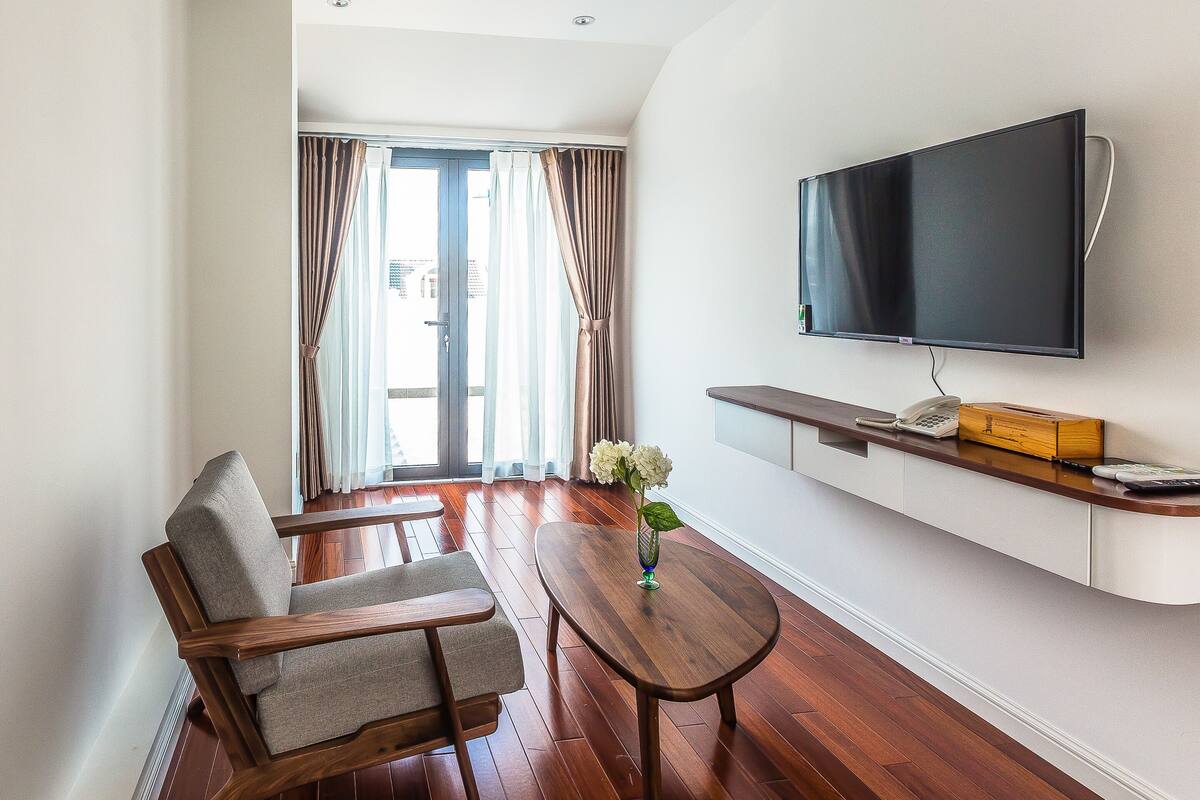Un salon moderne avec un téléviseur à écran plat fixé au mur, une table basse en bois, un canapé gris et une fenêtre avec des rideaux.