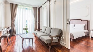 Quarto de hotel com piso de madeira, um sofá, uma cama, uma mesinha e uma cadeira.