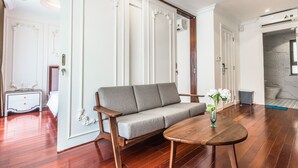 Uma sala de estar moderna com um sofá cinzento, mesa de centro de madeira e uma porta branca com molduras decorativas.