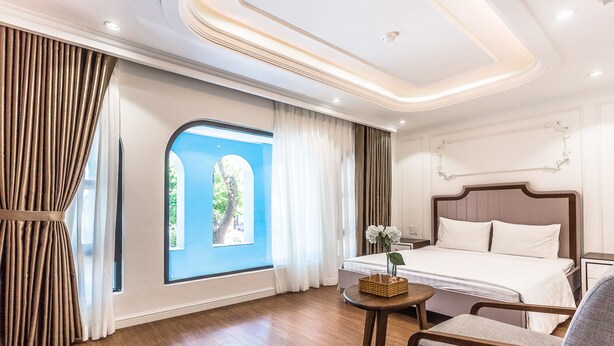 Quarto de hotel com uma janela grande, uma cama, uma cadeira e uma mesa pequena com uma cesta.