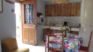 Un comedor con una mesa dispuesta para cuatro personas, sillas de madera, un sillón amarillo y un mantel con estampado floral.