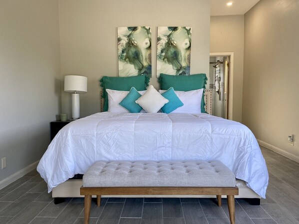 A bedroom with a large bed, a bench, a nightstand, a lamp, and two abstract paintings on the wall.