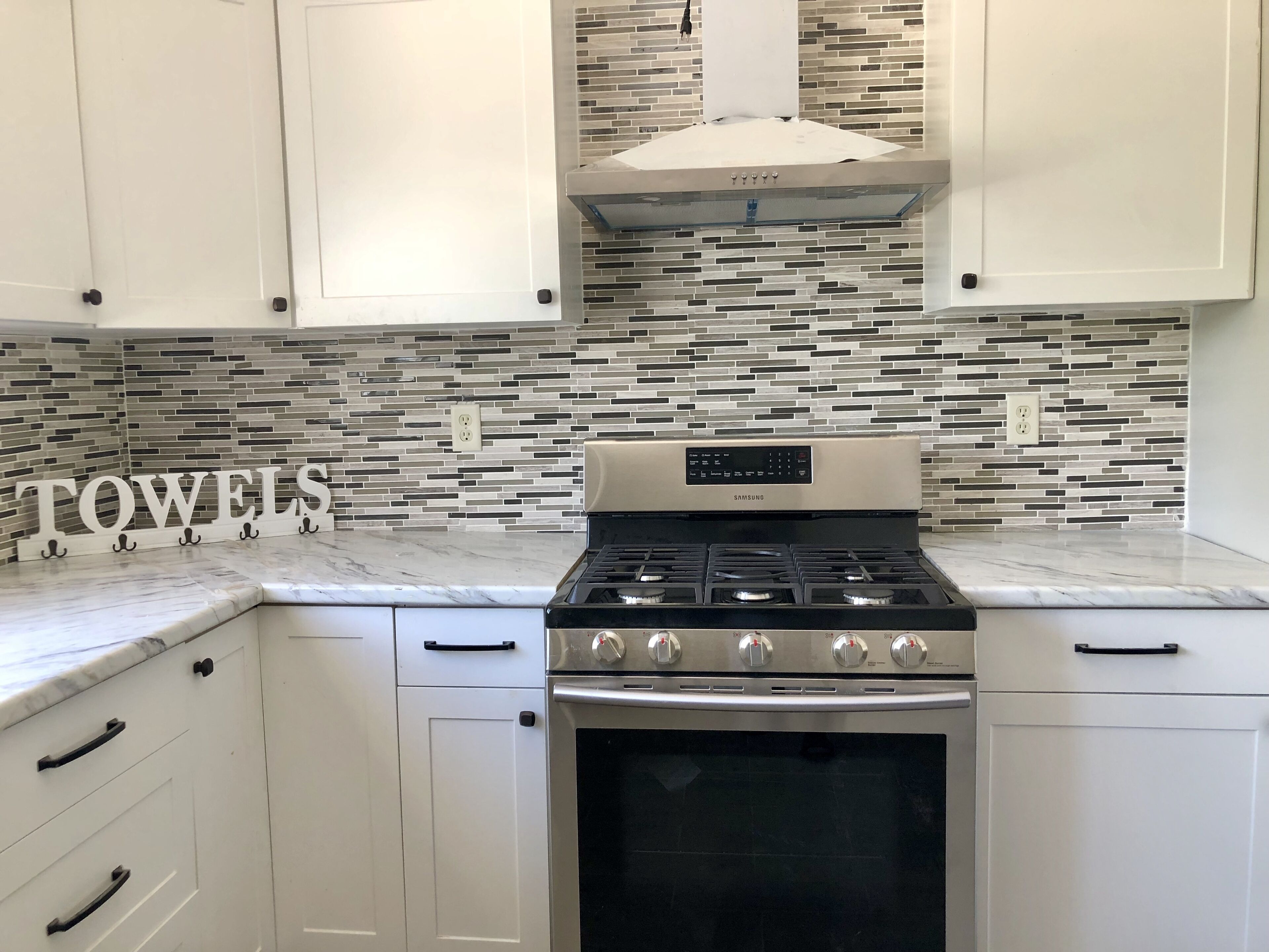 Una cocina con armarios blancos, estufa de acero inoxidable y salpicadero de azulejos.
