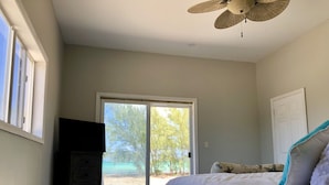 Een slaapkamer met een bed, een dressoir, een plafondventilator, een schuifdeur naar een terras en een witte deur.