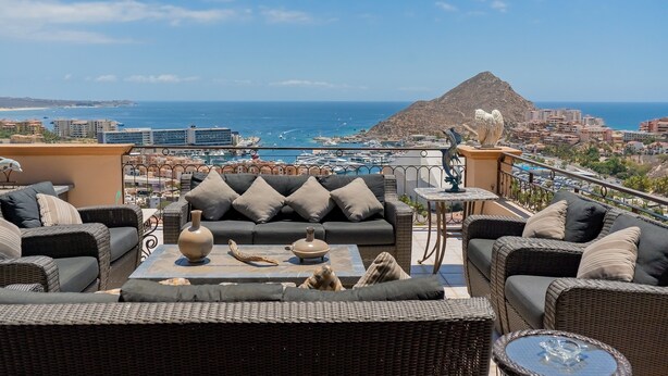 Una terraza en la azotea con muebles de mimbre, vistas al mar y una montaña en la distancia.
