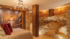 Un dormitorio con una cama grande, vigas de madera, paredes de piedra y un candelabro.