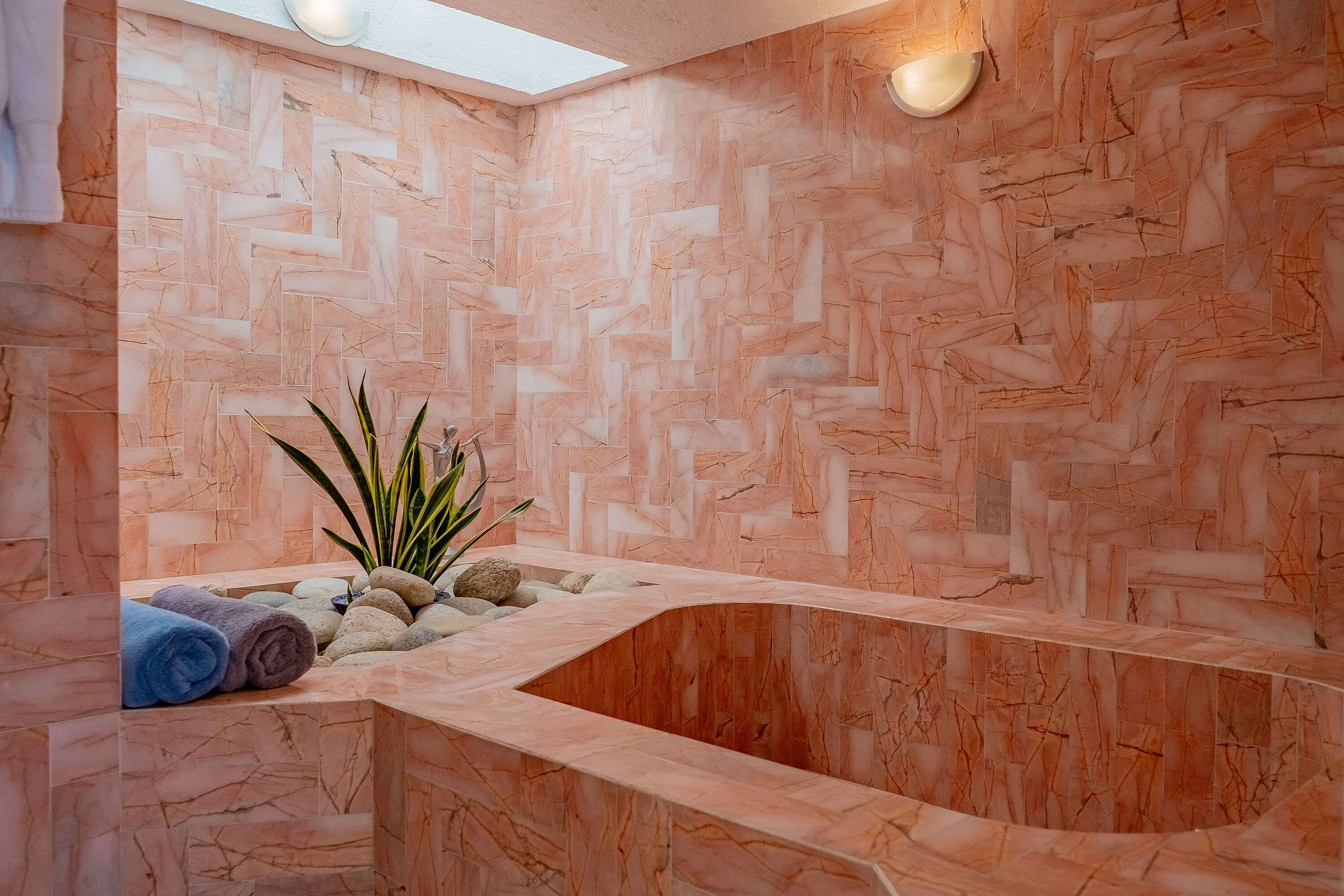Un área de spa con pared de mármol, un banco curvo y una planta.