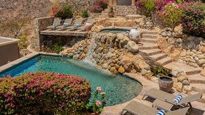 Un área de piscina con un jacuzzi, sillones de descanso y una cascada.