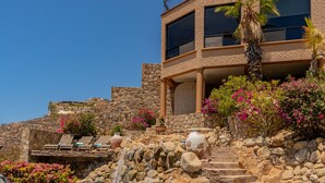 Un edificio de piedra con balcón, una palmera y flores rosas.