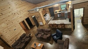 Un vaste espace intérieur aux murs en bois et au plafond haut. On y trouve plusieurs coins salon avec des canapés et des fauteuils, une table à manger et un coin cuisine visible au fond.